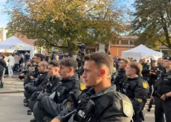 Polizeibeamte bei einem öffentlichen Einsatz während des D-Talk Festivals in einer Stadt, moderne Polizeiuniformen, Einsatz im Freien, im Hintergrund eine Menschenmenge und Zelte, Fokus auf Sicherheit bei Veranstaltungen.