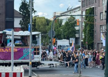 Menschenkette bei einer Demonstration in urbaner Umgebung mit Banner, Straßenabsperrungen und hohem Besucheraufkommen.