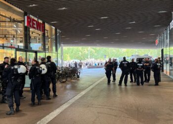 Große Gruppe von Polizeibeamten vor einem Einkaufszentrum während eines Einsatzes in Deutschland. Die Beamten tragen Schutzhelme und sind in einer Versammlung im Eingangsbereich.