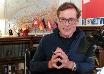 Hintergrund mit Reportage-Bücherschrank, Flaggen, und einem Moderator bei D-Talk, bekannt für politische Diskussionen und Interviews, bei der Arbeit im Studio.